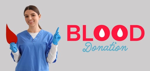 Wall Mural - Banner for World Blood Donor Day with young female nurse holding paper drop