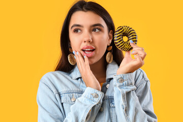 Wall Mural - Beautiful young woman with donut on yellow background