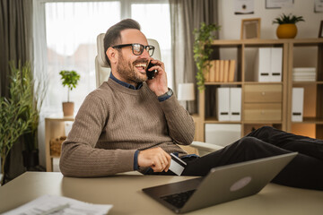 Adult businessman talk on mobile phone and hold credit card at office