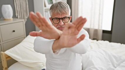 Wall Mural - Grey-haired, middle-aged man in pyjamas angrily rejects, wearing a stern expression and crossed arms in the bedroom