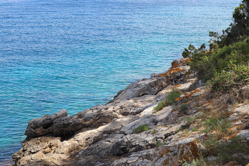 Rocky shore cliff with the some greenery in shade by the blue sea