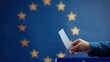 © Koplexs-Stock - European Union election, a voter's hand casts a ballot into a box against a blue backdrop featuring the European map and a flag adorned with twelve yellow stars