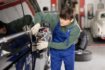 Wall Mural - Young guy mechanic in uniform inspects car door in car service station