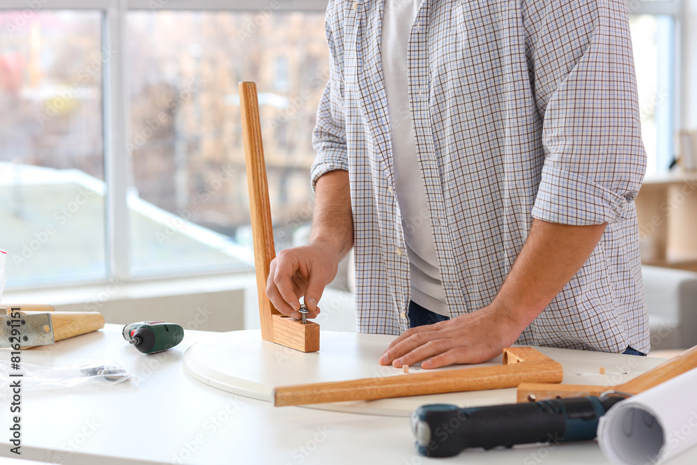 Young man with bolt assembling coffee table at home, closeup