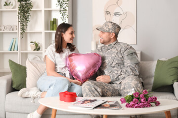 Wall Mural - Man in military uniform greeting his wife with heart-shaped balloon at home. Valentine's Day celebration