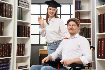 Wall Mural - Male graduate in wheelchair with his classmate at library