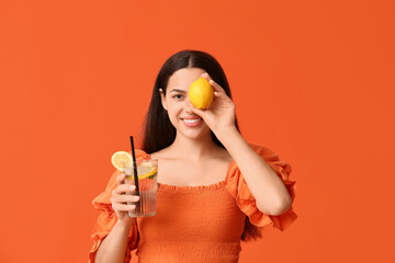 Poster - Beautiful young happy woman with lemon and glass of fresh lemonade on orange background