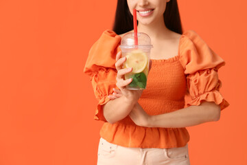 Poster - Beautiful young happy woman with cup of fresh lemonade on orange background, closeup