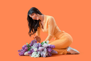 Poster - Beautiful young woman with lilac flowers sitting on orange background