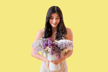 Poster - Beautiful young woman with lilac flowers in vase on yellow background