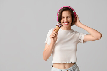 Poster - Beautiful young woman in headphones with sweet ice-cream in waffle cone on grey background