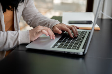 A woman typing on her laptop keyboard, working on her laptop computer at a table indoors.