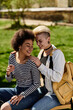 © Bliss - Two young women, lesbian couple, sit peacefully on a bench in a park, surrounded by lush greenery and the sounds of nature.