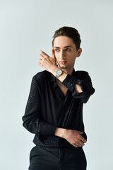 Wall Mural - A young man in a black shirt exudes confidence while posing in a studio setting against a grey background, embracing his LGBT identity.