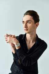 Wall Mural - A young man in a black shirt confidently displays his queer pride as he strikes a pose in a studio against a grey background.