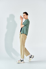Wall Mural - A young queer person in a green shirt and khaki pants stands confidently in front of a white wall in a studio setting.