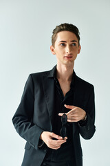 Wall Mural - A young queer person in a stylish black suit strikes a confident pose against a grey studio backdrop.