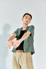 Wall Mural - A young queer person striking a confident pose in a studio, wearing a green shirt and tan pants against a grey background.