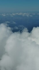 Wall Mural - Flying through beautiful white fluffy clouds in sky over blue sea. Airplane travel background. Vertical video