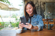 © Farknot Architect - Portrait image of a young woman holding and using mobile phone in cafe