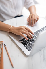 a close-up image of a woman typing on keyboard, working on the computer at a table in a coffee shop.