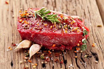 Canvas Print - Raw beef steaks with herbs and spices ready for cooking are on wooden board.