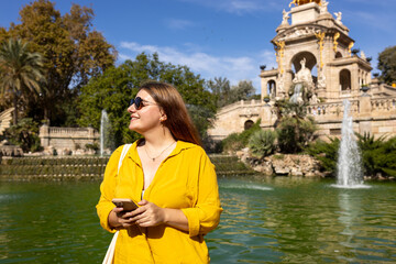 Wall Mural - Young female tourist with phone visiting Ciutadella Park in Barcelona. Concept of travel, tourism and vacation in city. Use technology concept, Traveling Europe