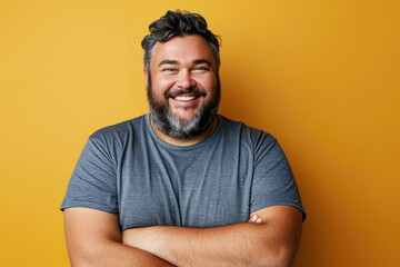 Wall Mural - Image of a happy fat man with arms crossed wearing a casual t-shirt on a mustard studio background