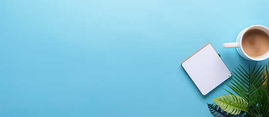 The copy space image shows a blue table background with a top view of an office desk It includes a notebook plastic plant smartphone and keyboard representing the concept of a creative designer