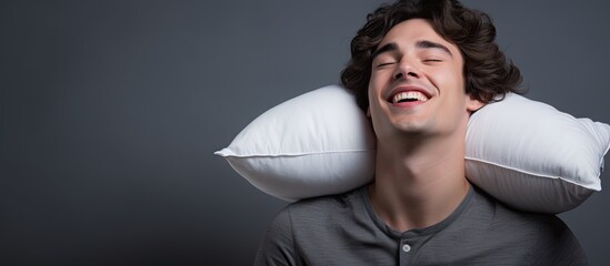 Poster - A young man with dark hair is giving a thumbs up while holding a white pillow against a grey background The image conveys the idea of sleep Copy space is available