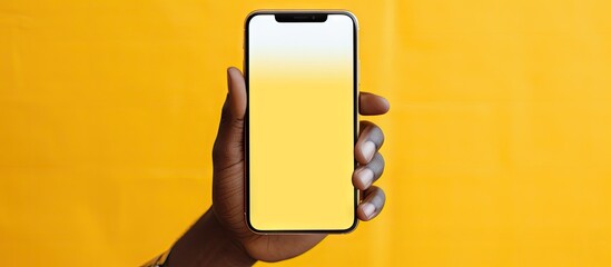 Poster - A stylish African man displaying a blank screen on his phone and indicating with his finger set against a blurry yellow background copy space image