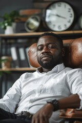 Poster - Man sitting in chair with clock in background, suitable for business or time management concepts