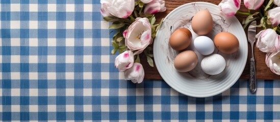 Poster - Easter table setting with white eggs in a nest on a blue and white checkered napkin Nearby are pink tulips Faces are painted on the eggs Copy space top view flat lay