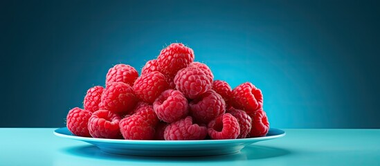 Poster - Bright ripe juicy raspberries on a gray plate on a blue background. copy space available