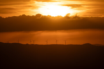 Wall Mural - Silhouette of wind turbines on the  mountain range under the dramatic sky at sunset