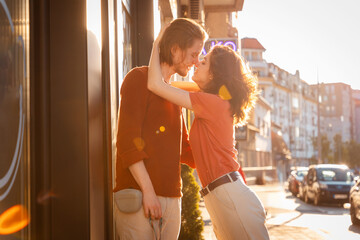 Side view of Young couple Caucasian man and woman, are kissing on street. Sunset light city in background. Psychology of relationship