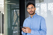 © Tetiana - Confident young professional in blue shirt holding smartphone at modern office