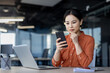 © Liubomir - Asian businesswoman seriously thinking while working in office, using phone and laptop. Focused at work.