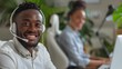 © Natalia - Smiling customer service representative wearing a headset, with a colleague in the background, working in a modern and vibrant office environment.