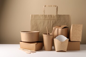 Wall Mural - Eco friendly food packaging. Paper containers, tableware and bag on white table against beige background