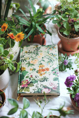 Poster - A notebook rests on a table surrounded by various potted plants and flowers