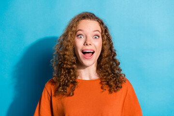 Wall Mural - Photo portrait of youth beautiful funny girl with curly hair wearing orange t shirt amazed reaction isolated on blue color background