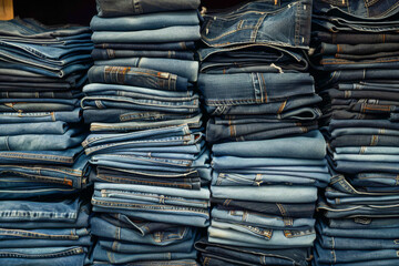 A pile of jeans stacked on top of each other. The jeans are all different sizes and styles