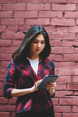 Wall Mural - Concentrated young hipster girl 20s holding modern touch pad in hands and searching information, attractive asian female student chatting with friends using 4g connection near copy space area