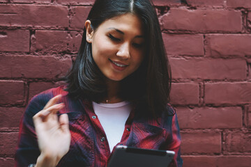 Wall Mural - Happy young hipster girl holding modern digital tablet and messaging while enjoying time near copy space area, cheerful female blogger using touch pad installing application and browsing 4g internet