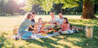 © Soloviova Liudmyla - Big family sitting on the picnic blanket in city park during weekend sunny day. They smiling, laughing and eating watermelon, boiled corn,pie with cold tea. Family values, outdoors activities concept.