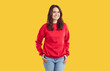 © Studio Romantic - Smiling young woman standing with her hands on hips. Portrait of beautiful brunette girl in red sweatshirt and jeans posing against yellow studio background. Positive emotions concept