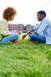 © BullRun - Two african american friends dressed in casual wear sitting against each other and communicating having conflict in relationship.Couple in love talking sitting on green grass in park