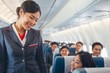 © polack - Asian woman stewardess smiling in a uniform is walking down the aisle of an airplane, smiling at the passengers. Happy Asian flight attendants in the airplane