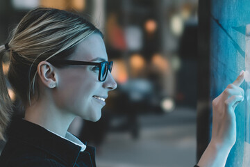 Wall Mural - smiling female standing at big display with advanced digital technology. young woman touching with f